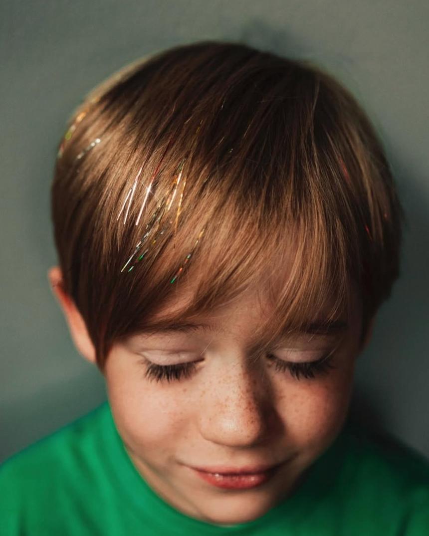 A young boy with prismatic sparkle strands through his fringe