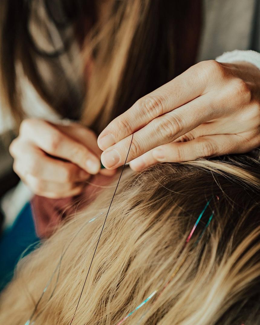 Two hands drawing a single fine strand into a section of hair at the root
