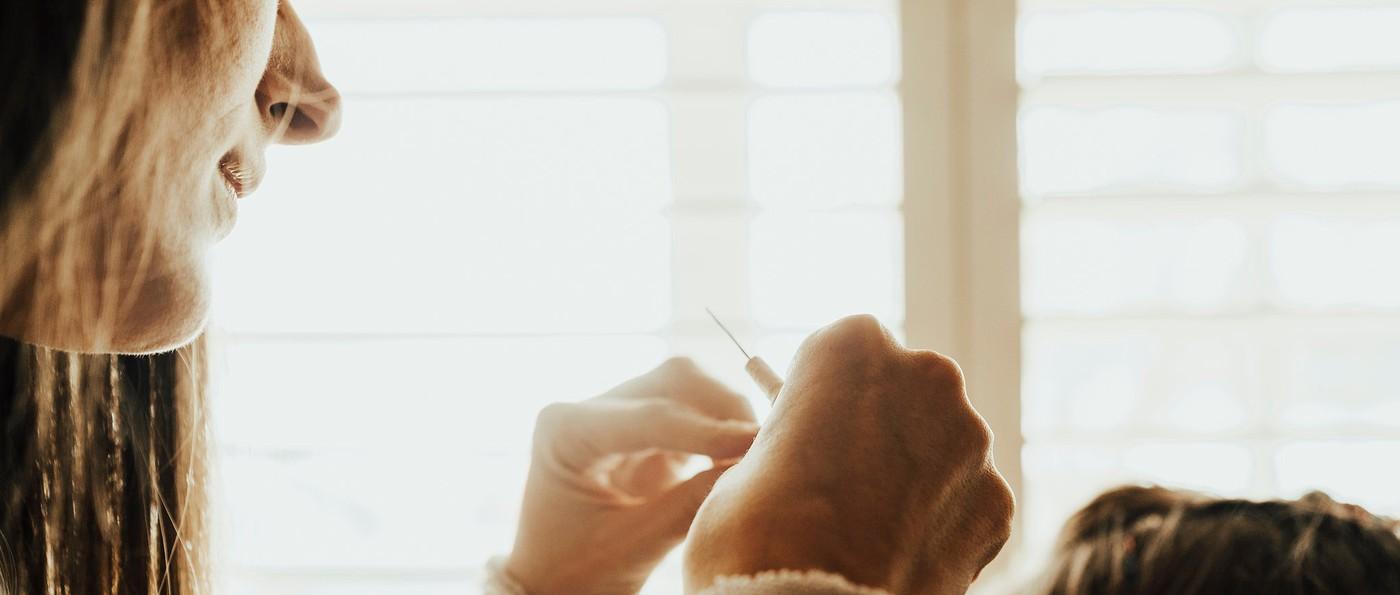 Backlit by a window, a hand draws the tying hook through a fine strand at the root