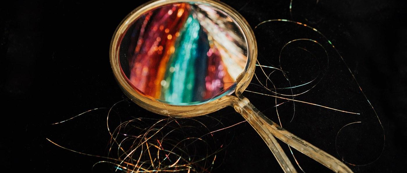 An antique hand mirror reflecting rows of sparkle colors, loose strands scattered around it